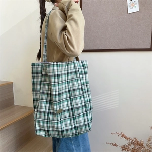 Detail of green and white plaid canvas tote bag showing the textured fabric and metal logo