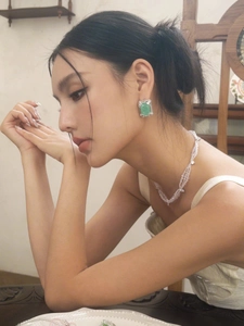 Close-up of a model wearing green square gemstone earrings with a pearl necklace