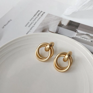 Detailed close-up of matte gold interlocking geometric hoop earrings on ceramic plate