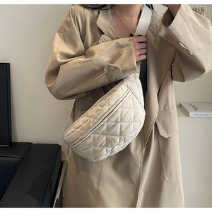 Detail of a beige quilted crossbody chest bag shown on a model wearing a trench coat