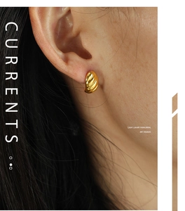Macro detail of golden C-shaped twisted horn earrings on model with metallic texture