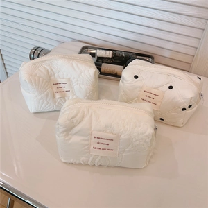 Détail de trousses à maquillage matelassées blanc crème avec broderies et étiquettes
