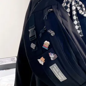 Dettaglio delle spille smaltate con gatti e libri su una borsa a tracolla in nylon nero