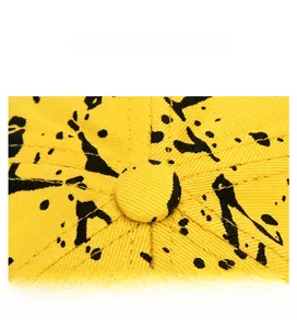 Close-up of yellow cotton baseball cap top featuring black ink splatter and detailed stitching