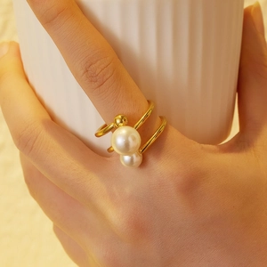 Close-up of gold double-ring with two white pearls worn by a model on a textured cup