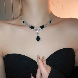 Close-up of a silver necklace with deep blue square and teardrop gems on a model