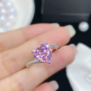 Foto macro de anillo plateado con gema de corazón rosa y piedras laterales brillantes