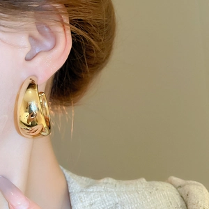 Close-up of elegant gold teardrop earrings with a glossy mirror finish on a female model