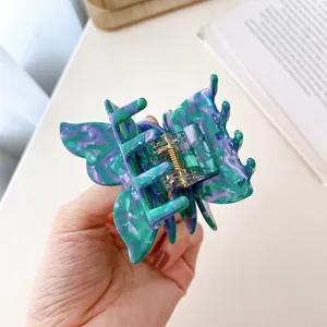 Acetate butterfly hair claw clip with green and purple marble texture held by hand