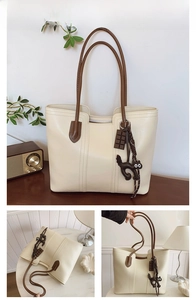 Detail of off-white tote bag with brown straps, black cat charm and chocolate pendant
