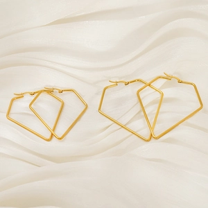 Detailed close-up of golden geometric hollow stud earrings on white soft fabric background