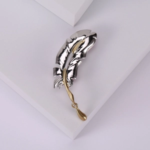 Elegant feather brooch pin in silver and gold tone on minimalist white display blocks