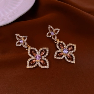 Close-up of golden hollow flower earrings with purple and peach stones and crystal details