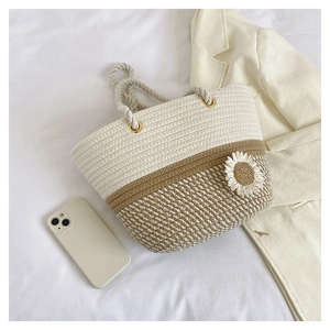 Detail of woven straw tote bag featuring a white 3D daisy flower and soft cotton rope handle