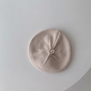 Close-up detail of the cream knit texture and top knot design on the baby beret hat