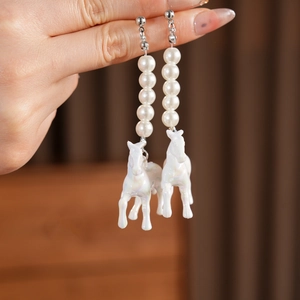 Macro shot of long drop earrings with white pearls and iridescent horse-shaped pendants