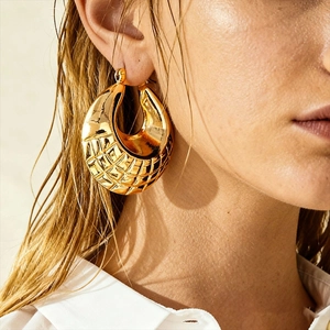 Close-up of model wearing gold chunky hoop earrings with textured geometric pattern