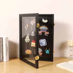 Black wooden pin display case with glass door and decorative brooches on a wooden desk