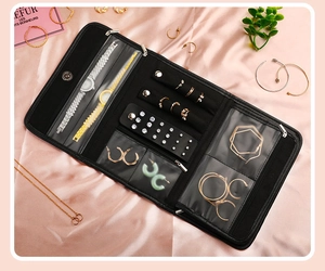 Flat lay of a black jewelry roll organizer with specialized compartments on pink silk