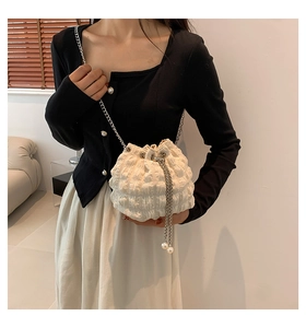 Detail of white pleated bucket bag featuring silver chain strap and pearl drawstring toggle