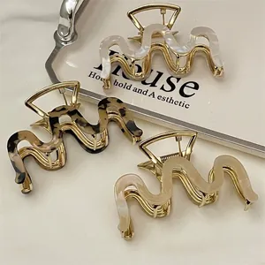 Three wave-shaped acetate hair claws in pearl white, amber, and beige with gold metal base