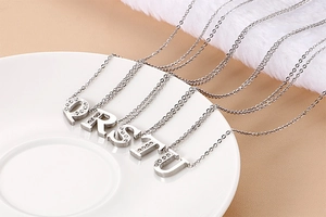 Close-up of silver-plated necklaces with crystal-encrusted letters Q R S T U on ceramic
