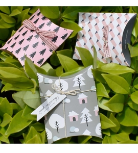 Detailed view of three decorative paper pillow gift boxes with ribbons on green leaves