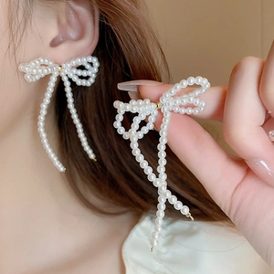 Elegant white pearl bow earrings with long tassels shown on ear and held by hand