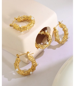 Détail de boucles d'oreilles C dorées avec texture martelée, perles et zircons