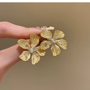 Close-up of golden metal flower earrings with crystal center and brushed texture
