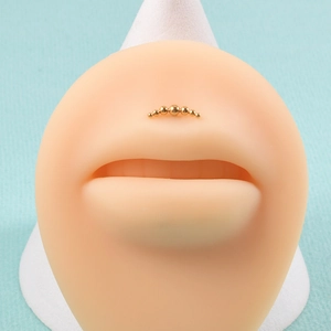 Detail showing gold beaded piercing jewelry on a facial model with multiple small gold balls
