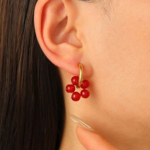 Close-up of gold hoop earring featuring red bead clusters on a model ear