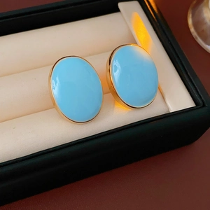 Macro shot of oval sky blue enamel earrings in gold settings inside a black jewelry box