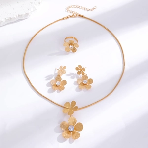Detail of gold floral jewelry set with textured petals and zircon center on white background