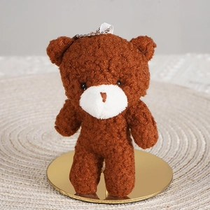 Close-up of curly brown plush bear keychain with metal ball chain on a golden stand