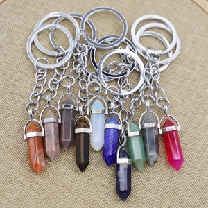Hexagonal crystal stone pillar keychains in various colors on a beige linen background