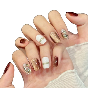 Brown and gold glitter press-on nails with star patterns and cream accents on hands