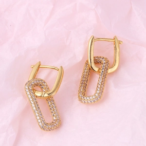 Minimalist gold geometric interlocking earrings with pink gemstones on pink paper