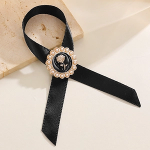 Gros plan sur broche nœud noir avec détail de rose dorée et bordure de perles