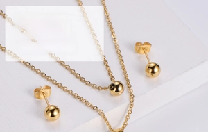 Detailed close-up of a minimalist gold plated titanium steel jewelry set with ball charms