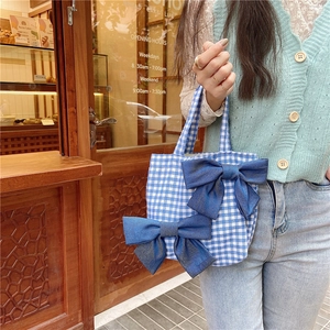Detail of blue plaid canvas tote bag featuring double denim bow accents in a vintage cafe