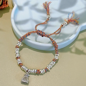 Detail of woven multi-color rope bracelet with silver metal charms and tassel