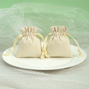 Detail shot of beige cotton drawstring pouches on white ceramic plate with soft lighting