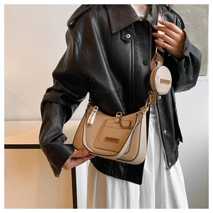 Detail of khaki saddle bag with round charm, golden chain, and faux leather texture
