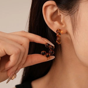 Detail of amber beaded C-shaped resin earrings shown on model with soft lighting