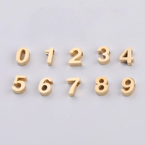 Dettaglio macro di ciondoli numerici 0-9 in acciaio dorato per la creazione di gioielli