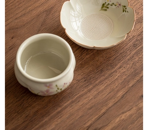 Detail of hand-painted ceramic tea strainer set with pink floral patterns and gold trim