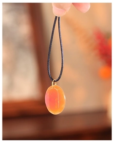 Détail d'un pendentif ovale facetté en résine avec dégradé orange-rose sur cordon