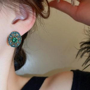 Close-up of vintage gold earrings with large green gemstone and blue pavé crystals