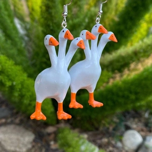 Close-up of creative three-headed white goose earrings with orange beaks and silver hooks